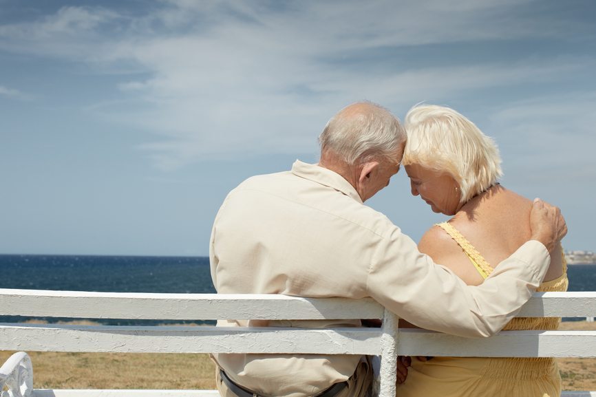 senior caucasian couple sitting on bench near the sea and hugging. Horizontal shape, rear view, copy space