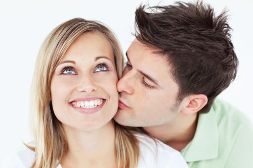 careful man kissing his smiling girlfriend against a white background
