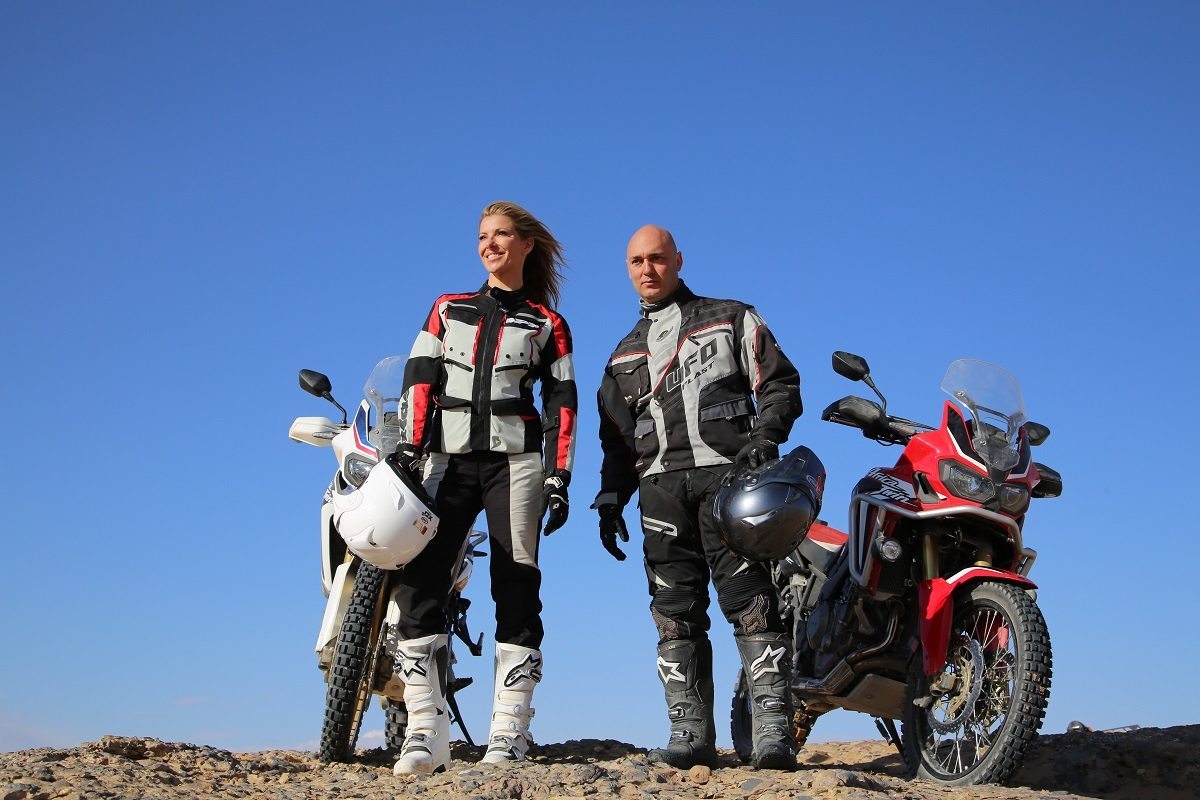 ERFOUD, Morocco - Laura and Christophe standing next to their motorbikes with their helmets in their hands. Clear blue skies. (Photo Credit: National Geographic Channels/Rebecca Hevingham)